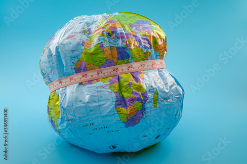 Global obesity epidemic crisis affecting increasing numbers of earth population and chronic health condition concept with globe and measuring tape isolated on blue background