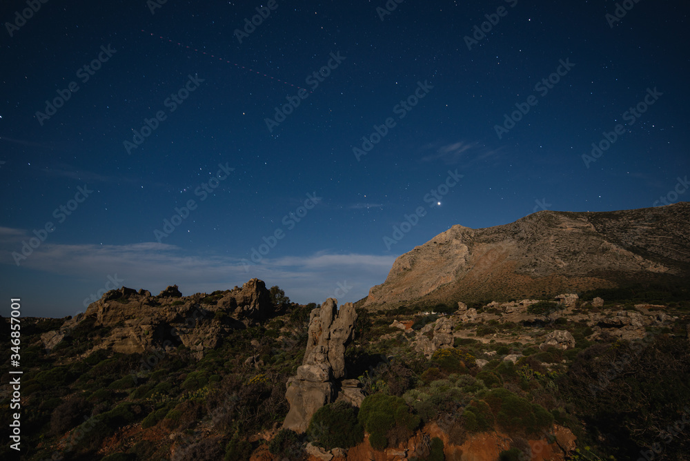 Night mountains view with star sky and full moon of the The petrified forest park in Lakonia, Peloponnese, Greece. View of petrified forest with plant fossils on star sky background.