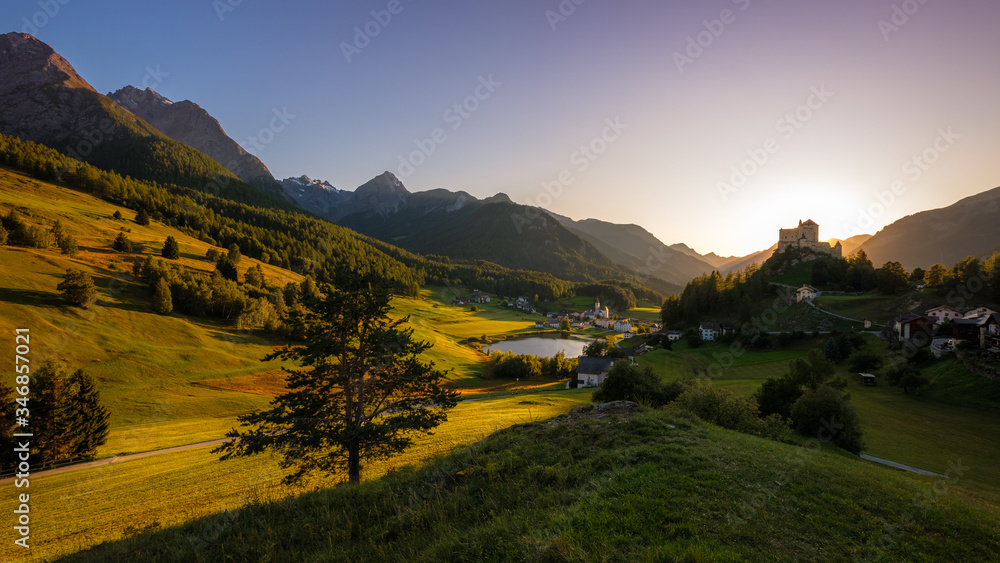 Fototapeta premium Sun is setting at the mountains surrounding Tarasp and its castle, in the canton of Graubünden (Engadin) Switzerland. The castle is a Swiss heritage site of national significance
