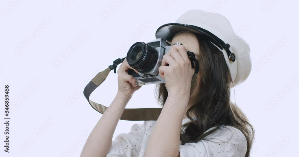 Close up of the beautiful and cute little Caucasian girl in a hat taking photos with a photocamera and then smiling cheerfully on the white wall background. Portrait. Close up of the beautiful and cute little Caucasian girl in a hat taking photos with a photocamera and then smiling cheerfully on the white wall background. Portrait.