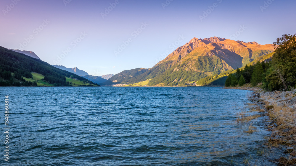 Sunset at Lake Resia (German: Reschensee) and the village of Resia in Val Venosta (Alto Adige, Italy). It lies next to Lake della Muta (German: Haidersee) and across the Austrian border at Resia Pass Sunset at Lake Resia (German: Reschensee) and the village of Resia in Val Venosta (Alto Adige, Italy). It lies next to Lake della Muta (German: Haidersee) and across the Austrian border at Resia Pass