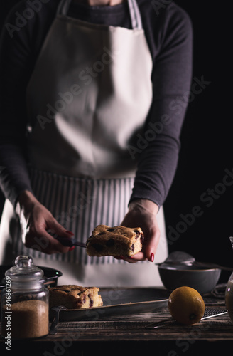 Close up of female chefs hands servicing slice of cake with cherries on dark background.