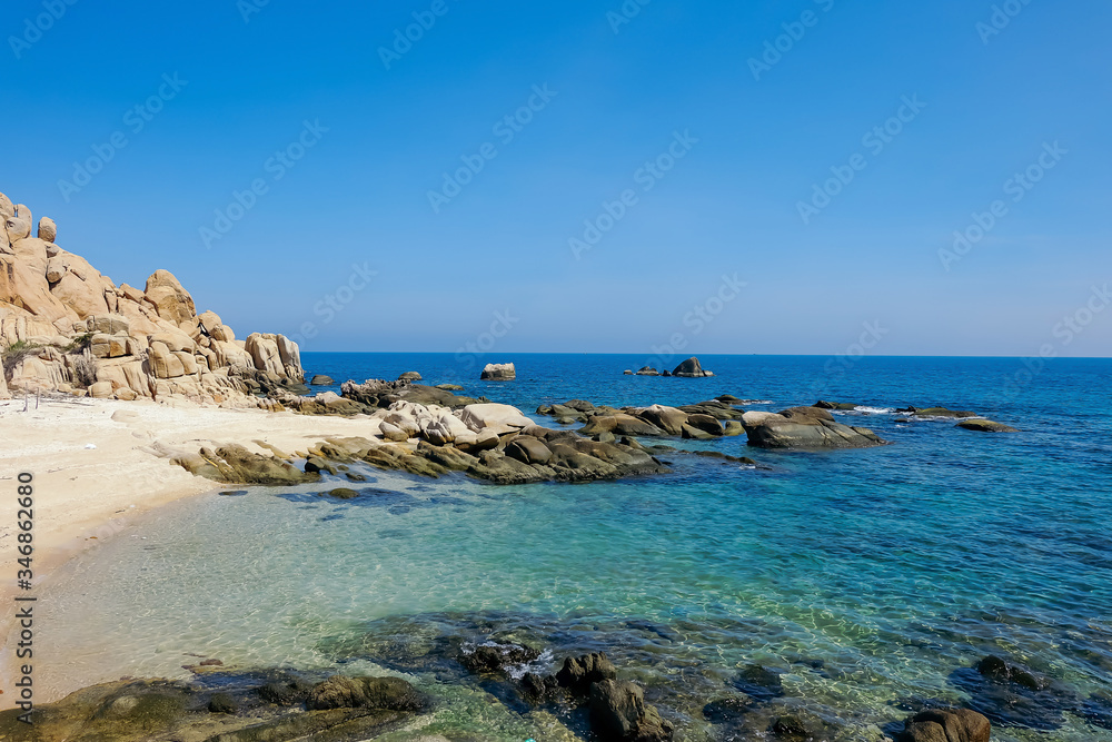 Beautiful seascape with blue sea, rocks, sand, and bright blue sky at a small island in Binh Thuan province, Vietnam. Royalty high-quality free stock image of the sea landscape.