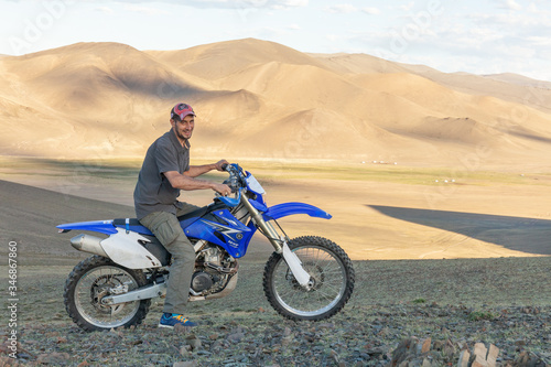 Fototapeta Naklejka Na Ścianę i Meble -  Altai, Mongolia - June 14, 2017: A happy motorcyclist is preparing a trip