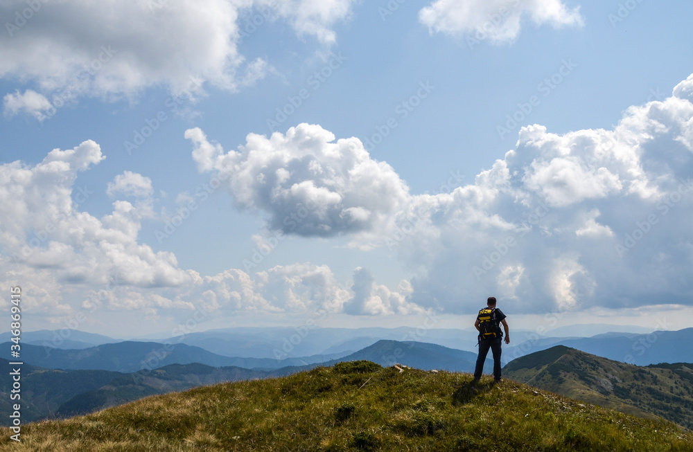 Hiker with backpack standing on a top of a mountain enjoying lookout view of mountains. Nature landscape in Carpathians. Healthy active lifestyle.