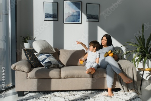 Cheerful mother sitting on couch in cozy light living room holds on lap tickles of little son enjoy funny activities on weekend at home, have fun together, priceless time with preschool child concept