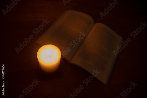 Candle burning brightly with open book on wooden table. Top down view.