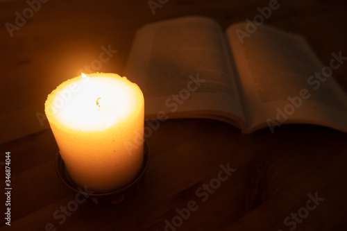 Candle burning brightly with book in background. Close up, shallow depth of field.