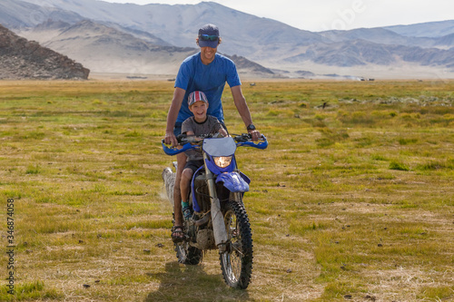 Father rides his son on a motorbike. The son is very happy.
