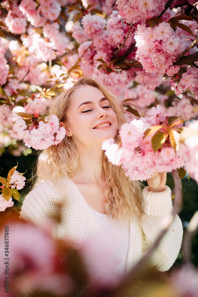 Fototapeta premium Portrait of young woman in park with blooming sakura trees.
