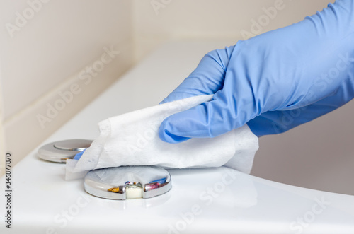 Woman with surgical gloves wiping the buttons on the jacuzzi bath with wet wipes .
