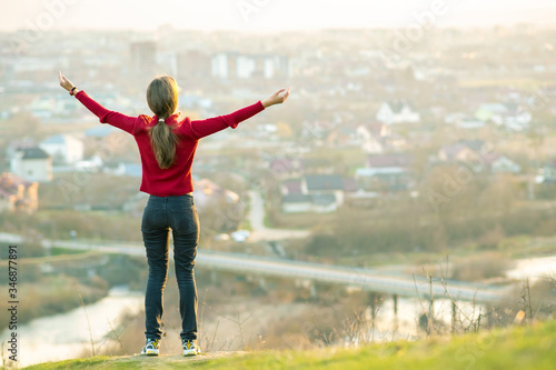 Young woman standing outdoors raising her hands enjoying city view. Relaxing, freedom and wellness concept.