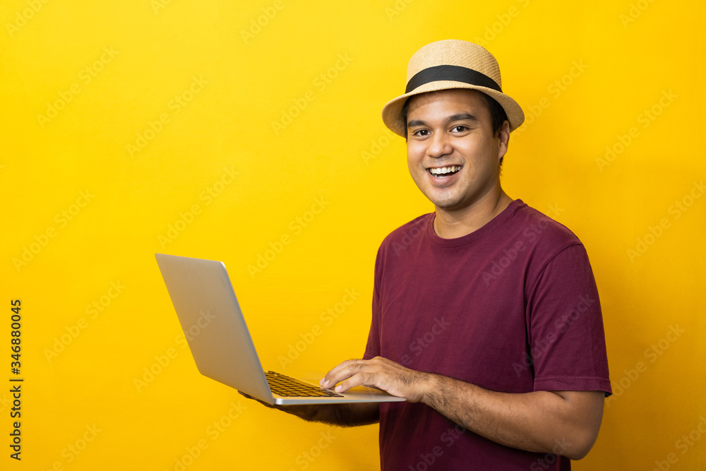 Asian man red shirt with hat using laptop on isolated yellow background.