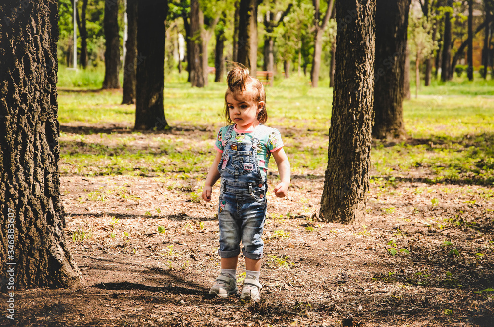 May 2020. Kiev Ukraine. A little girl plays outside in a park, collects plants on a sunny day in denim overalls and a T-shirt with a print LOL May 2020. Kiev Ukraine. A little girl plays outside in a park, collects plants on a sunny day in denim overalls and a T-shirt with a print LOL