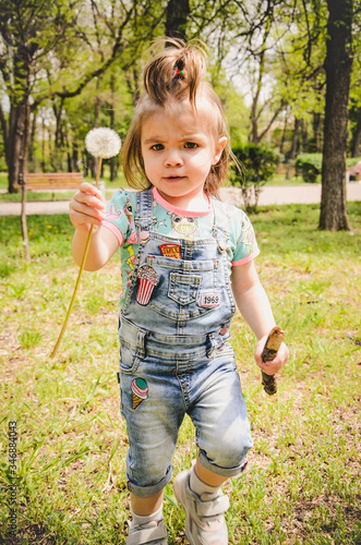 May 2020. Kiev Ukraine. A little girl plays outside in a park, collects plants on a sunny day in denim overalls and a T-shirt with a print  LOL