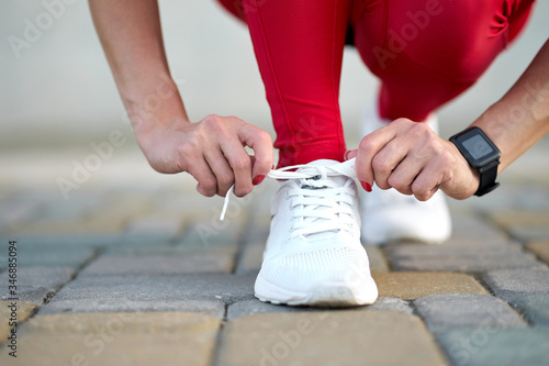 Closeup of female legs in stylish red sport leggings and trendy white sneakers. Active slim woman on a training. Get ready for start.