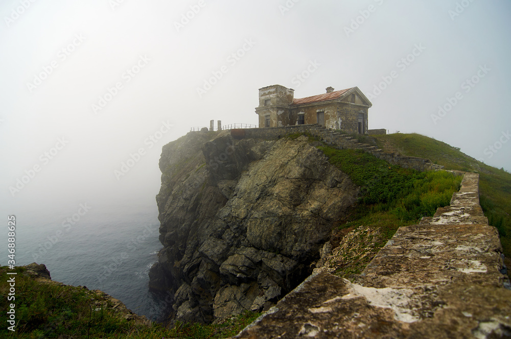 Old lighthouse in the fog on a cliff by the ocean. Gamow Lighthouse on the Gamow Peninsula. Dangerous Bay in the Sea of Japan. Far East.