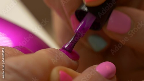 Painting nails with hybrid varnish in a beauty salon. Pink and purple nail polish