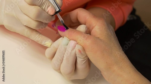 Beautician in protective gloves paints nails