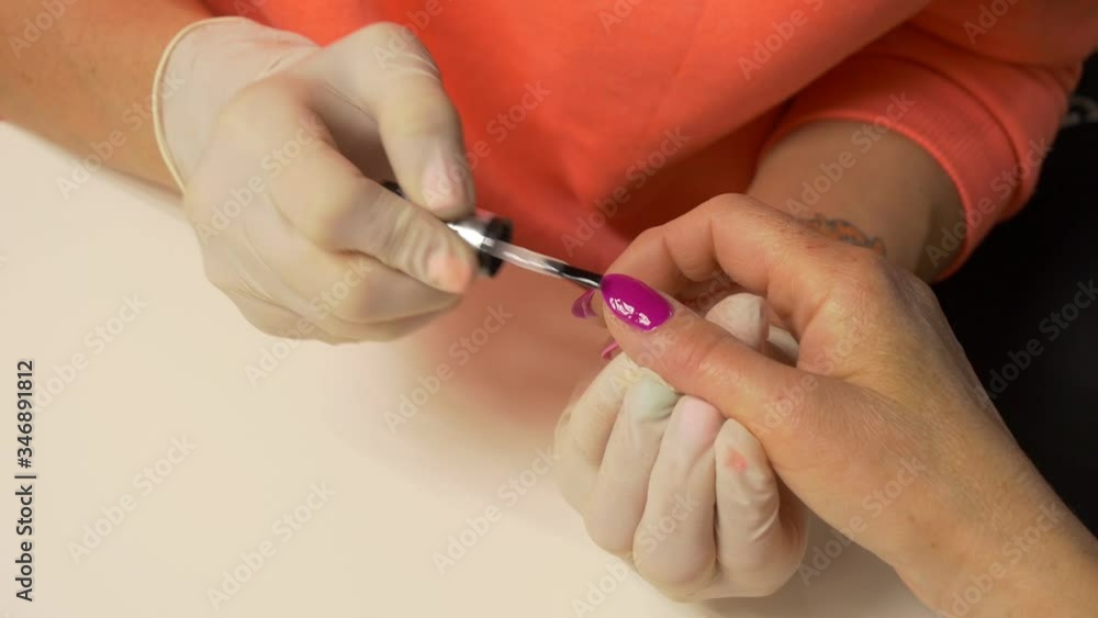 Beautician in protective gloves paints nails