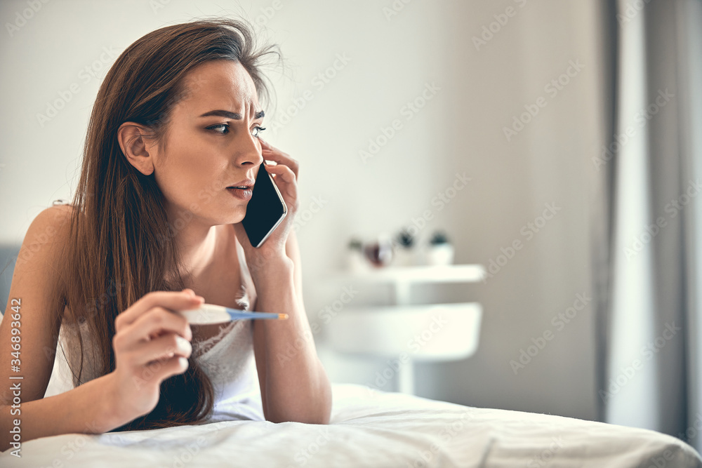 Caucasian scared lady checking her temperature with thermometer at home Caucasian scared lady checking her temperature with thermometer at home