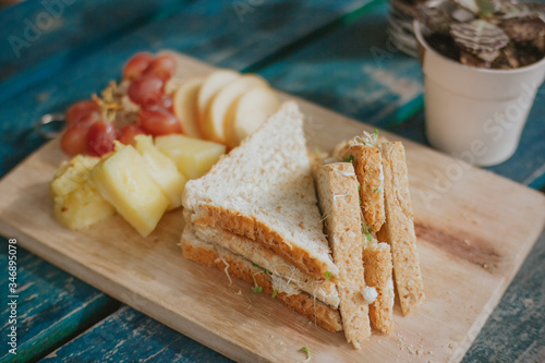 A sandwich cut in half with fruits on a wood panel. Rustic.