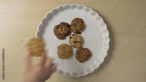 Female hands arrange cookies on a plate. Several people take cookies from the plate.
