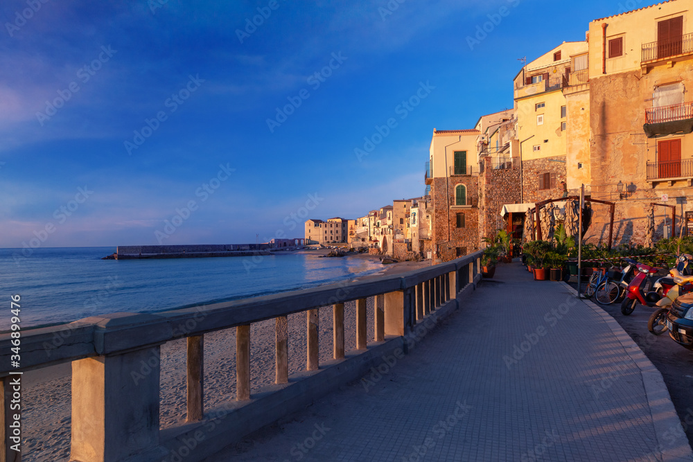 Tourist promenade and empty beach in old town of coastal city Cefalu at sunset, Sicily, Italy