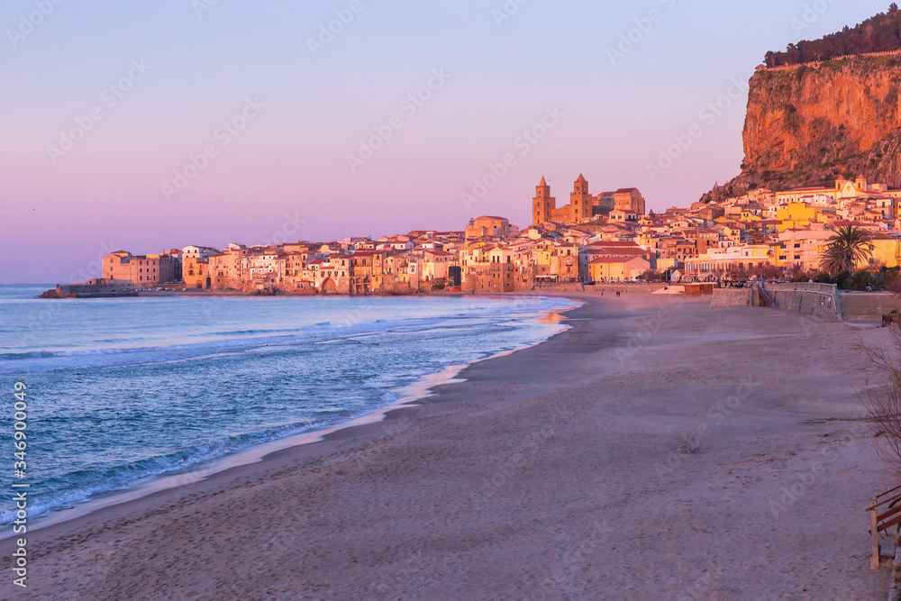 Beautiful view of empty beach, Cefalu Cathedral and old town of coastal city Cefalu at pink sunset, Sicily, Italy