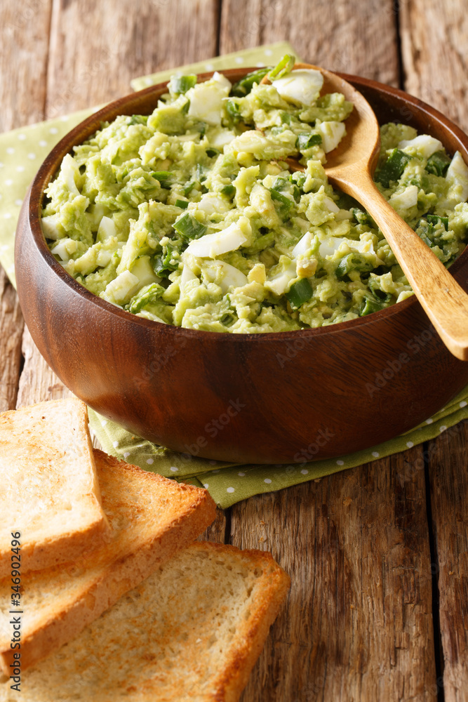 Fresh salad of avocado mashed with boiled eggs and green onions in a bowl close-up. vertical Fresh salad of avocado mashed with boiled eggs and green onions in a bowl close-up. vertical
