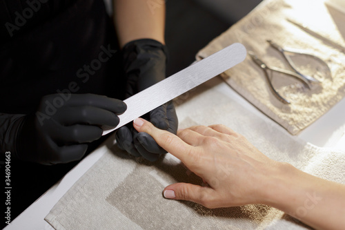 dettaglio di manicure con lima usata dall'operatrice che indossa i guanti neri verso una cliente che porge la mano