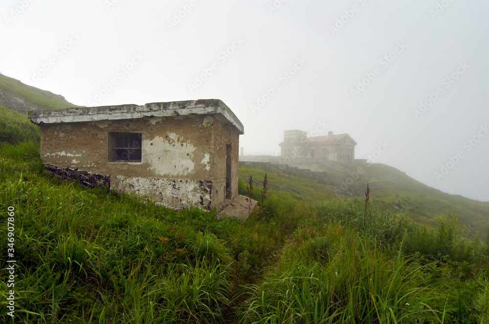 Old lighthouse in the fog on a cliff by the ocean. Gamow Lighthouse on the Gamow Peninsula. Dangerous Bay in the Sea of Japan. Far East. Old lighthouse in the fog on a cliff by the ocean. Gamow Lighthouse on the Gamow Peninsula. Dangerous Bay in the Sea of Japan. Far East.