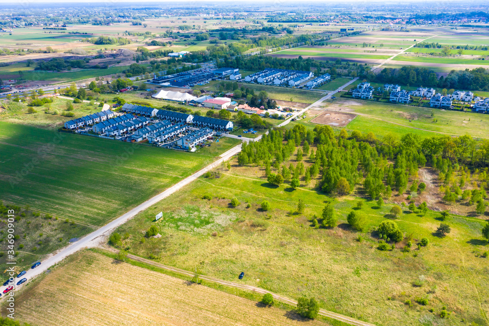 Aerial view of residential houses neighborhood and apartment building complex at sunset. Tightly packed homes, driveway surrounds green tree flyove. Suburban housing development