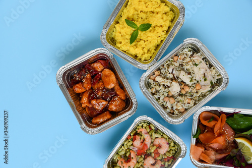 Food delivery. Different aluminium containers with healthy diet natural food. Top view on blue background.