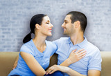 Portrait picture of young happy smiling attractive amorous embracing couple, looking at each other, over white brick loft style wall, indoors.
