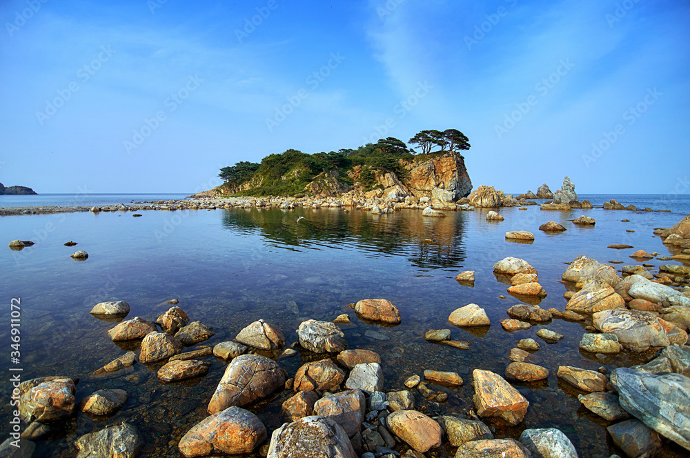 Rocky high island in the ocean. Rocky high island in Orlik Bay in the Sea of Japan. In the foreground are stones and clear water. Far East.