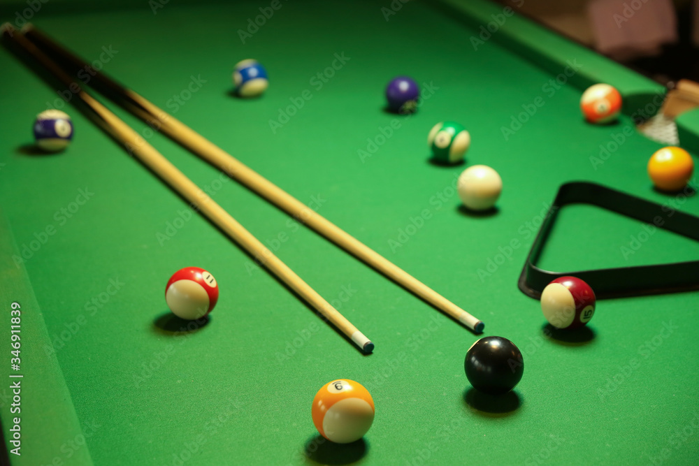 billiard cues and multicolored pool balls on green billiard table