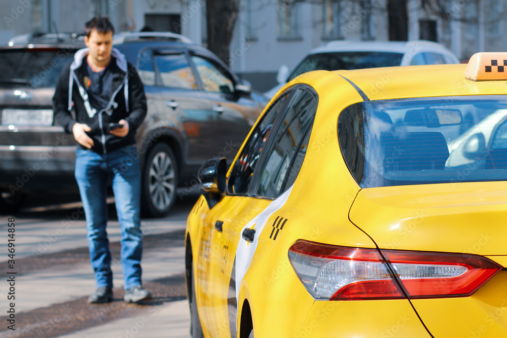 The taxi stopped in front of the man who had called the car. It checks the car number in the phone app. Blurred background. The taxi stopped in front of the man who had called the car. It checks the car number in the phone app. Blurred background.