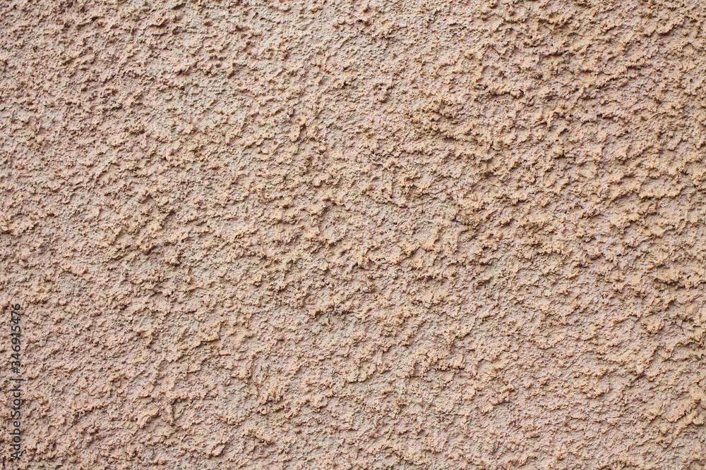 A rough beige wall, plastered with concrete. Visible spots and stripes. The surface is grey with bumps and hollows. A rough beige wall, plastered with concrete. Visible spots and stripes. The surface is grey with bumps and hollows.