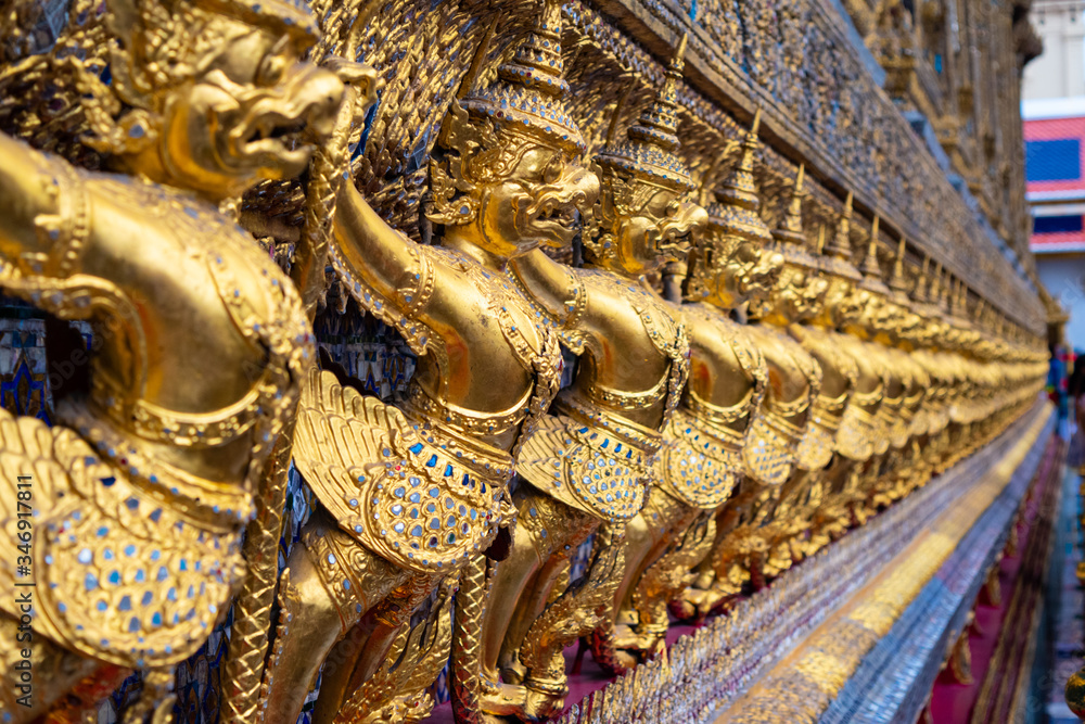 Exterior side decoration made with  thai mosaic and small statues of golden warrior demon at the Grand Palace in Bangkok, Thailand