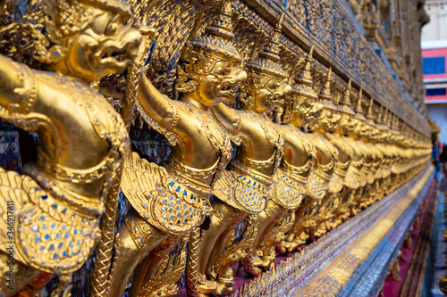 Exterior side decoration made with  thai mosaic and small statues of golden warrior demon at the Grand Palace in Bangkok  Thailand