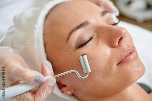 Female receiving electric facial treatment by cosmetologist wearing gloves professional services.