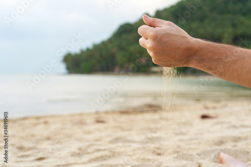 Play with sand on the beach. Sand is poured from the hands, against the backdrop of a tropical island. © Kate