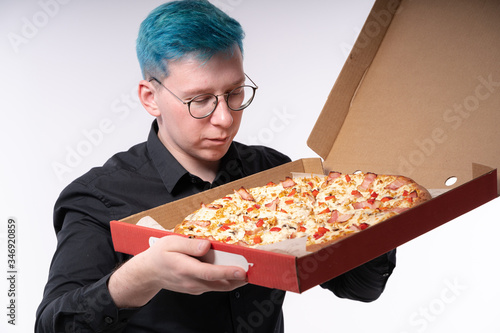 Close up of a stylish young man with blue hair, holding pizza and staring at it with a great desire, studio shooting on light background photo