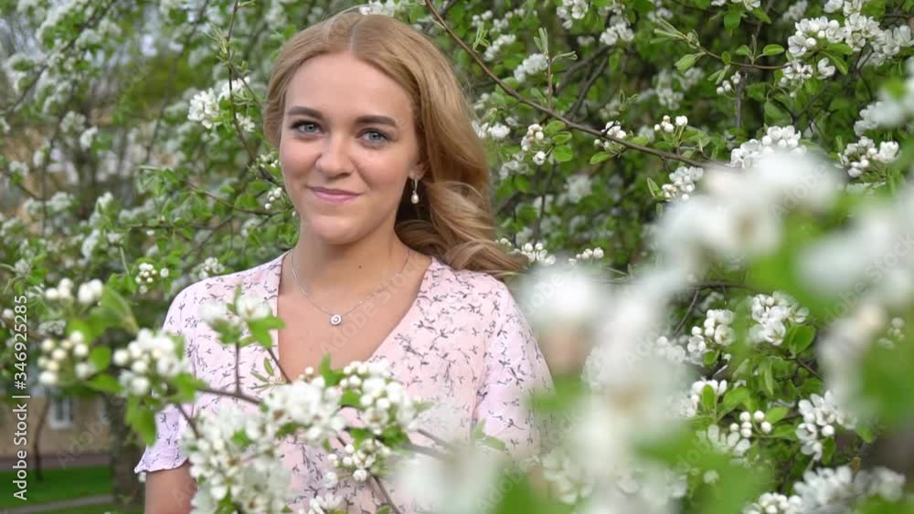 young attractive woman with long blonde hair at the beautiful blooming sakura garden. Happy Beautiful girl in blooming trees. Beautiful blonde girl posing in blooming tree branches with white flowers