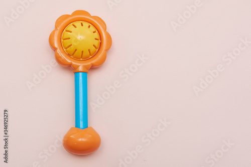 Plastic toy rattle in bright yellow color with a blue handle. Plastic Retro Rattle. Baby toys on pink background. Flat lay. Copy space.