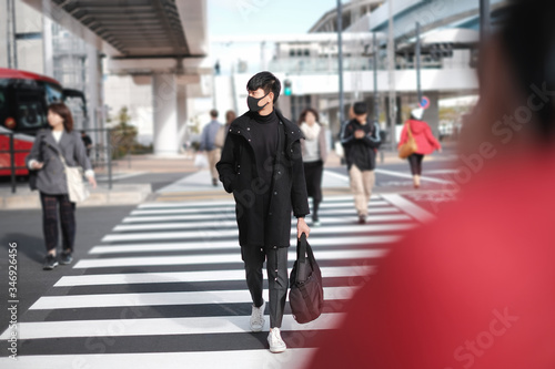 Man wearing black surgical mask and carrying bag crossing road to other side in big city and photo shooting model concept
