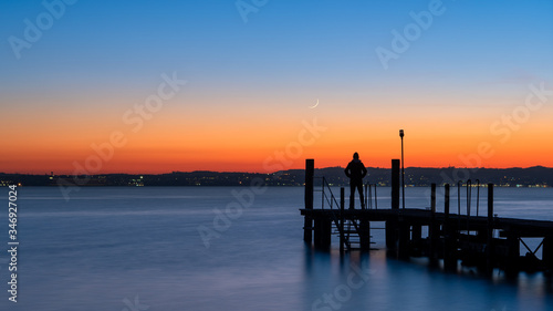 A man silhouette standing on wooden pier lonely at the sea with beautiful sunset. lsunset seascape at a wooden jetty. © Davide Marconcini