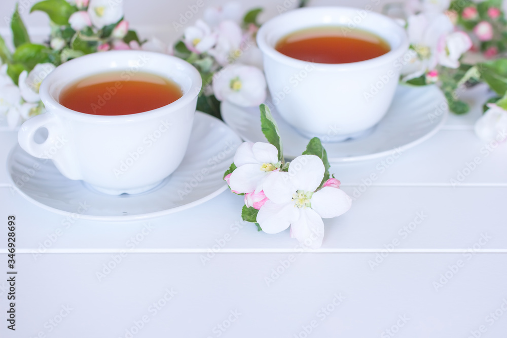 two cups of tea and spring white flowers on a white background. spring background with cups of tea and branches of white flowers. two cups of tea and spring white flowers on a white background. spring background with cups of tea and branches of white flowers.