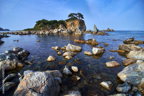Rocky high island in the ocean. Rocky high island in Orlik Bay in the Sea of Japan. In the foreground are stones and clear water. Far East.